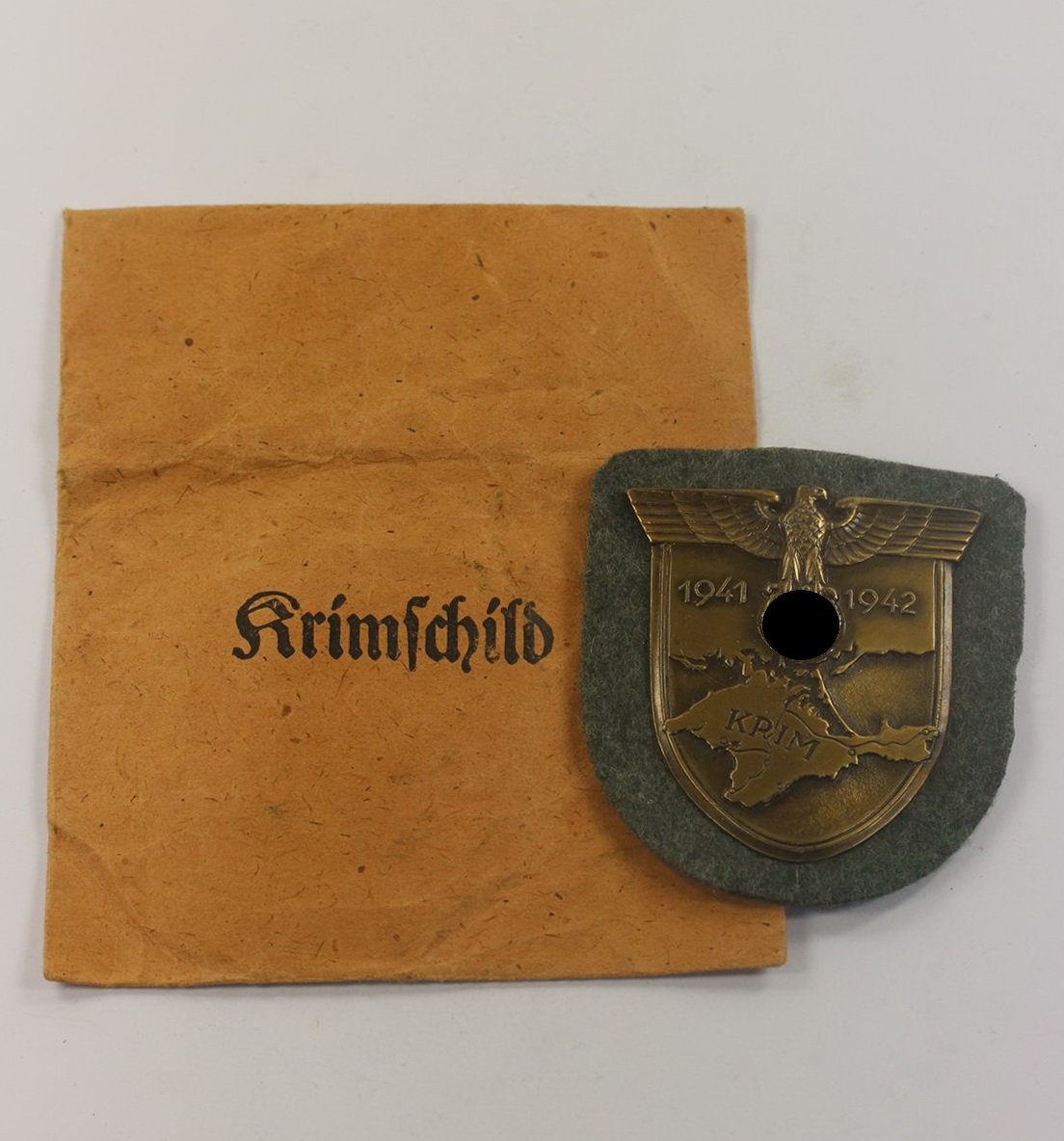 Krimschild auf Heeresstoff, in Verleihungstüte, Friedrich Orth Wien 56 (1) Krimschild auf Heeresstoff, in Verleihungstüte, Friedrich Orth Wien 56 – Bild 1